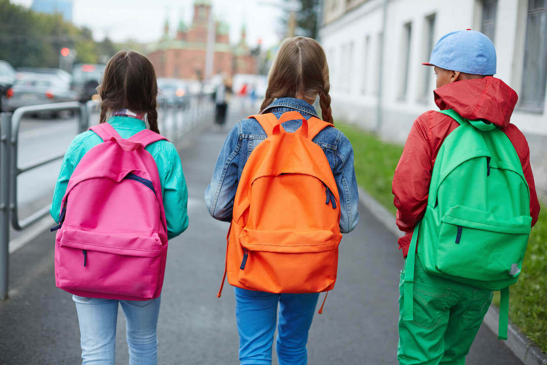 three children walking to school with bright colored backpacks